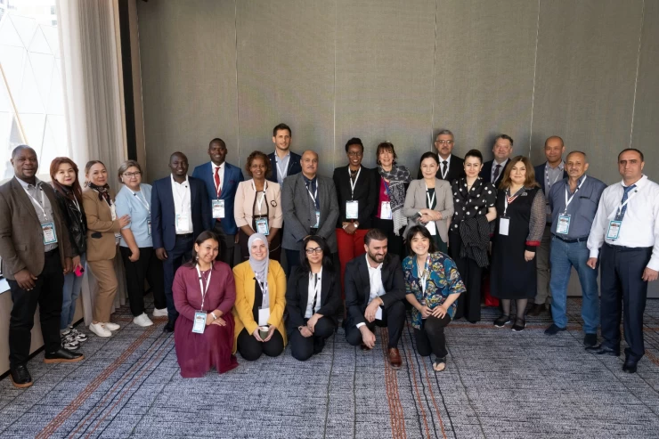 A large gathering of people from many nations stand in an arch, with 5 kneeling in front. They are members of the Capacity Building and Implementation Support countries and liaison officers.